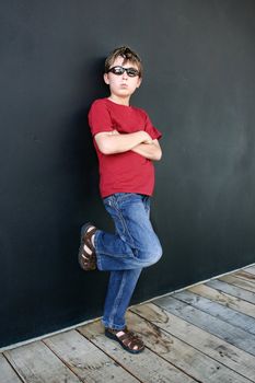 Child in jeans and t-shirt stands casually leaning partially against the wall behind him. Added contast.