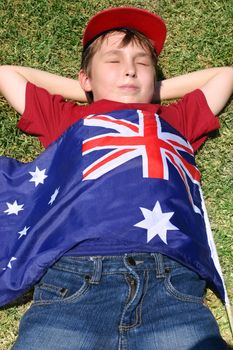 Patriotic boy with flag draped over him laying in park.