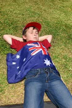 Patriotic Australian boy with Australian flag taking a short rest on grassy area.