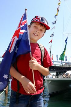 Young aussie boy proudly holding flag by the harbourside mariner on Australia Day national holiday.