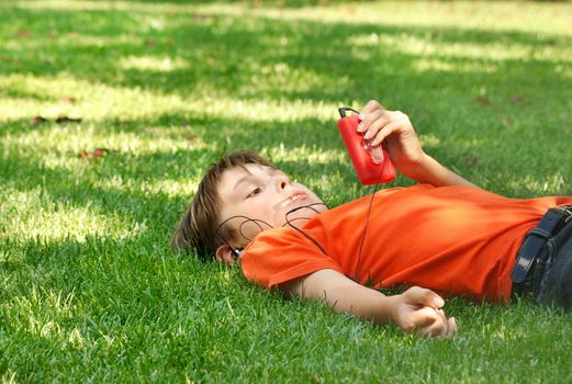 A boy relaxing and listening to music on mp3 player in the dappled shade of a tree in the park
200 @ f5.6