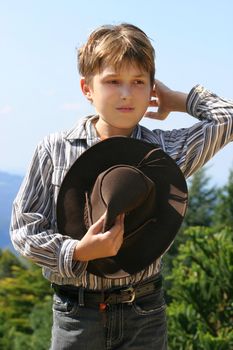 Outback rural boy in magnificent high country, holding hat, whilst rustling hair and looking out over the field on a sunny day.