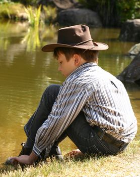 A young boy sits and plays by the edge of an outback billabong