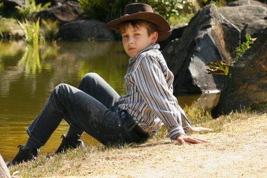 Young rural boy sitting on the banks of a small river inlet in outback Australia.