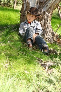 A boy from the bush sits under the shade of an Australian gum tree.  200iso