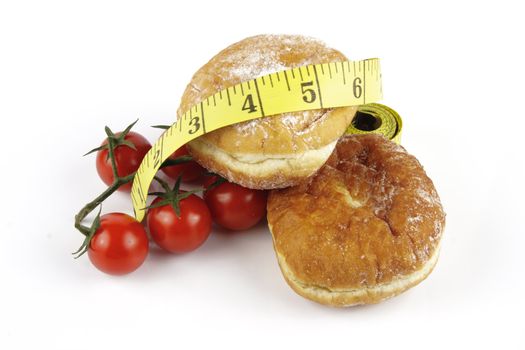 Contradiction between healthy food and junk food using red ripe tomatoes and doughnuts with a yellow tape measure on a reflective white background 