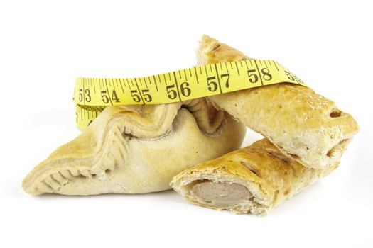 Single golden sausage roll cut in half with pasty and yellow tape measure on a reflective white background