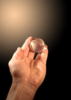 Glass globe lying at human hand on gradient background with copy space