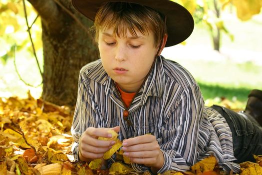 A child lays in golden yellow autumn foliage under a deciduous tree - 400iso