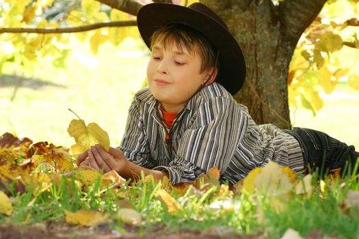 A child resting under a deciduous tree and playing with fallen autumn leaves.   The process of leaves changing colour is called  photoperiodism, the ability of plants to measure length of light and adjust accordingly - please note 400iso f7
