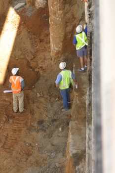 Three construction workers, one holding blueprints, on an excavation site
