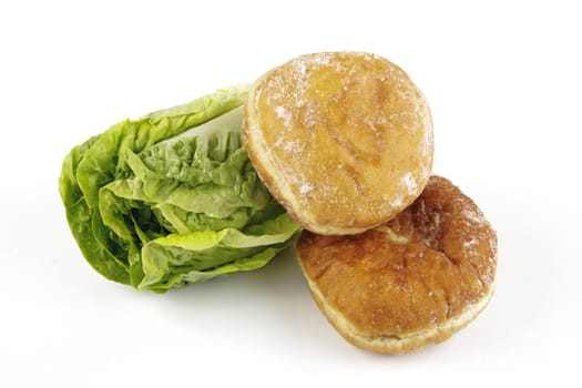 Contradiction between healthy food and junk food using a green salad lettace and jam doughnut on a reflective white background 