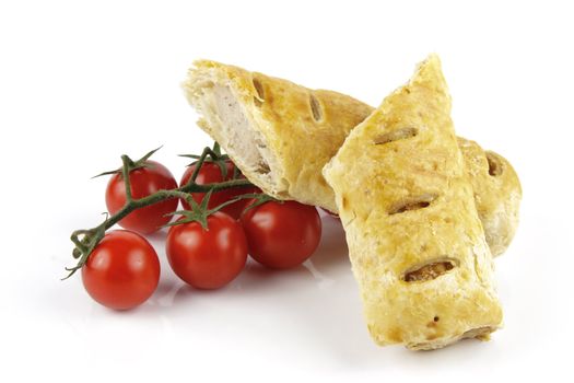 Contradiction between healthy food and junk food using tomatoes and a sausage roll on a reflective white background 