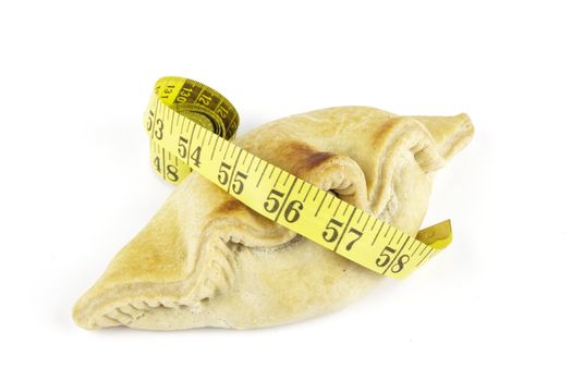 Single golden pasty and yellow tape measure on a reflective white background