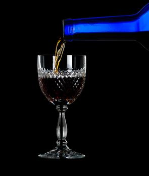 Sherry, port or whisky being poured from blue wine bottle into an elegant cut glass and isolated against black