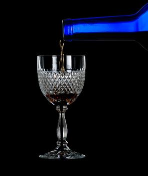 Sherry, port or whisky being poured from blue wine bottle into an elegant cut glass and isolated against black