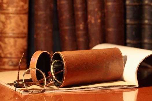 Closeup of old spectacles inside leather case on background with book