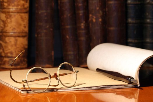 Vintage still life with old spectacles, paper notebook and pen on background with books