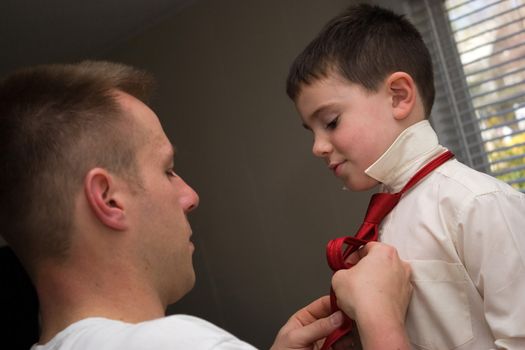 A young dad helps his son get ready by helping him tie his neck tie.