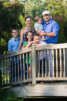 Portrait of an attractive young family with four children posing in a park on a wooden walking bridge.
