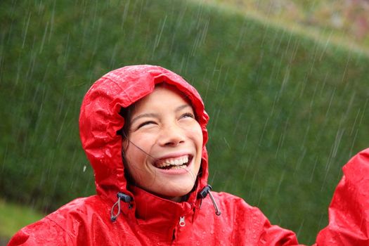Young woman wearing a red raincoat enjoying the rain and having fun outside. 