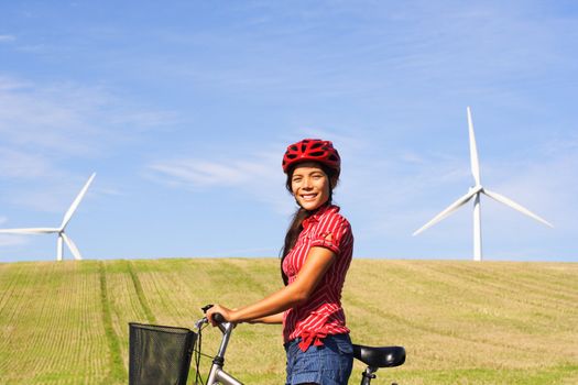 sustainable future concept. Girl on bike with field and wind turbines. Blue sky with copy space. Beautiful mixed asian / caucasian model.