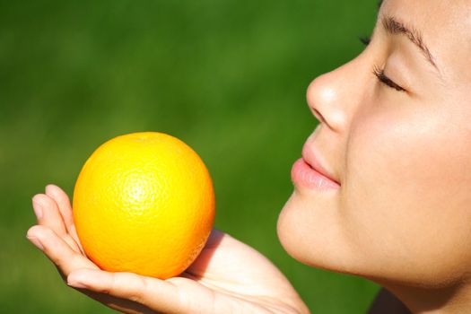 Beautiful mixed race chinese / caucasian woman enjoying the smell of an orange during summer.