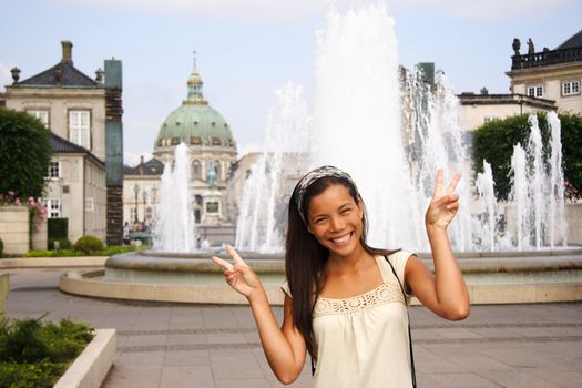 Young woman doing peace sign while visiting the city of Copenhagen, Denmark during summer. Beautiful mixed race chinese / caucasian model.