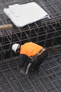 A builder secures steel mesh.  Various site plans rest nearby.
