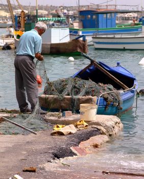 Old fisherman fixing his nets at the fishing village of Marsaxlokk in Malta