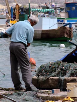 Old man and the sea - fisherman fixing his nets at the fishing village of Marsaxlokk in Malta