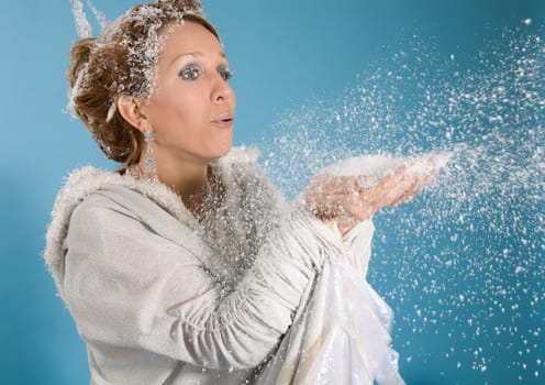 Beautiful blond woman dressed in an elegant robe blowing snow from her hands