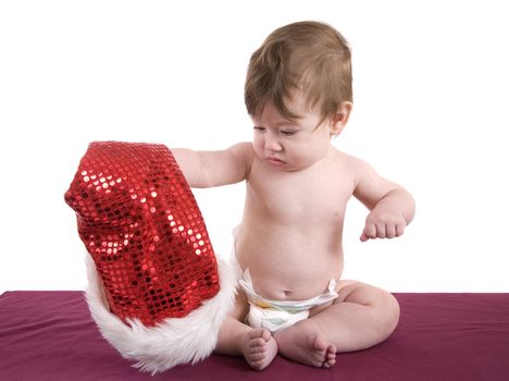 Cute baby girl looking at the santa hat in her hand wondering what to do with it