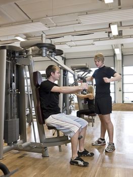 Man instructing how to use an exercise machine with a young woman in the background