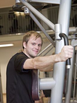 Young man using an exercise machine at a health club with a girl and a boy in the background