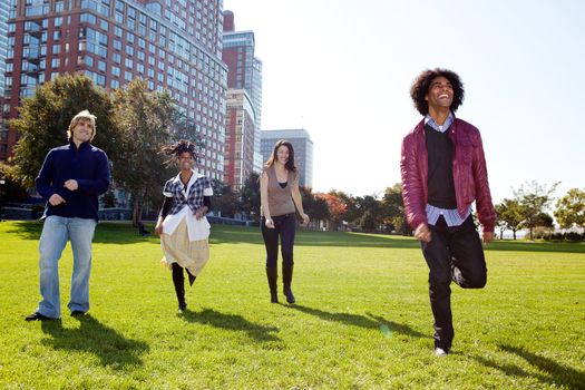 A group of happy people running towads the camera.  Sharp focus on rear three people, motion blur on front person.