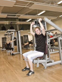 Young man using an exercise machine at a health club with a girl and a boy in the background