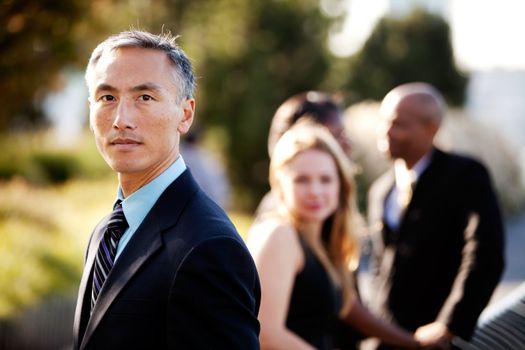 An Asian business man with a serious expression and colleagues in the background