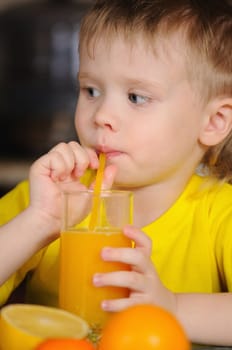 The child in a yellow vest drinks  orange juice