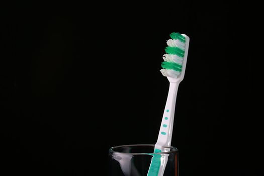 New dark green with white a tooth-brush in a glass on a black background.