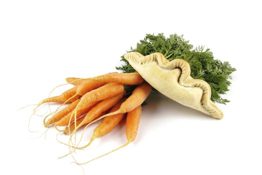Contradiction between healthy food and junk food using bunch of carrots and pasty on a reflective white background 