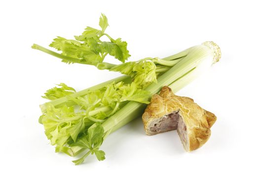 Contradiction between healthy food and junk food using celery and pork pie on a reflective white background 