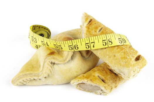 Single golden sausage roll cut in half with pasty and yellow tape measure on a reflective white background