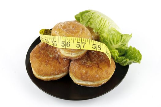 Contradiction between healthy food and junk food using doughnuts and lettace with a tape measure on a reflective white background 