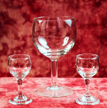 Two small and one large glass goblets are empty against a red background