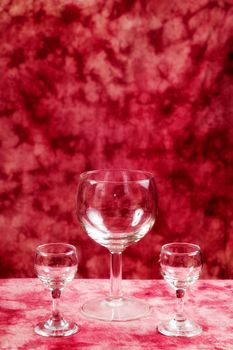 Two small and one large glass goblets are empty against a red background