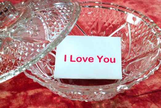 A love letter sitting in a glass candy dish which says, "I love you"