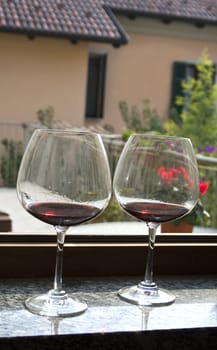 Two glasses of red wine over an open window