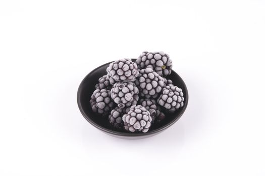 Black ripe frozen blackberries in a small round black dish with a reflective white background