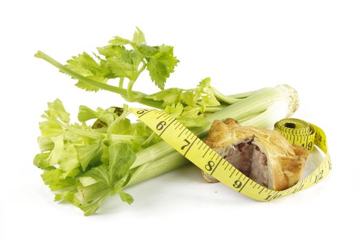 Contradiction between healthy food and junk food using celery and pork pie with a tape measure on a reflective white background 